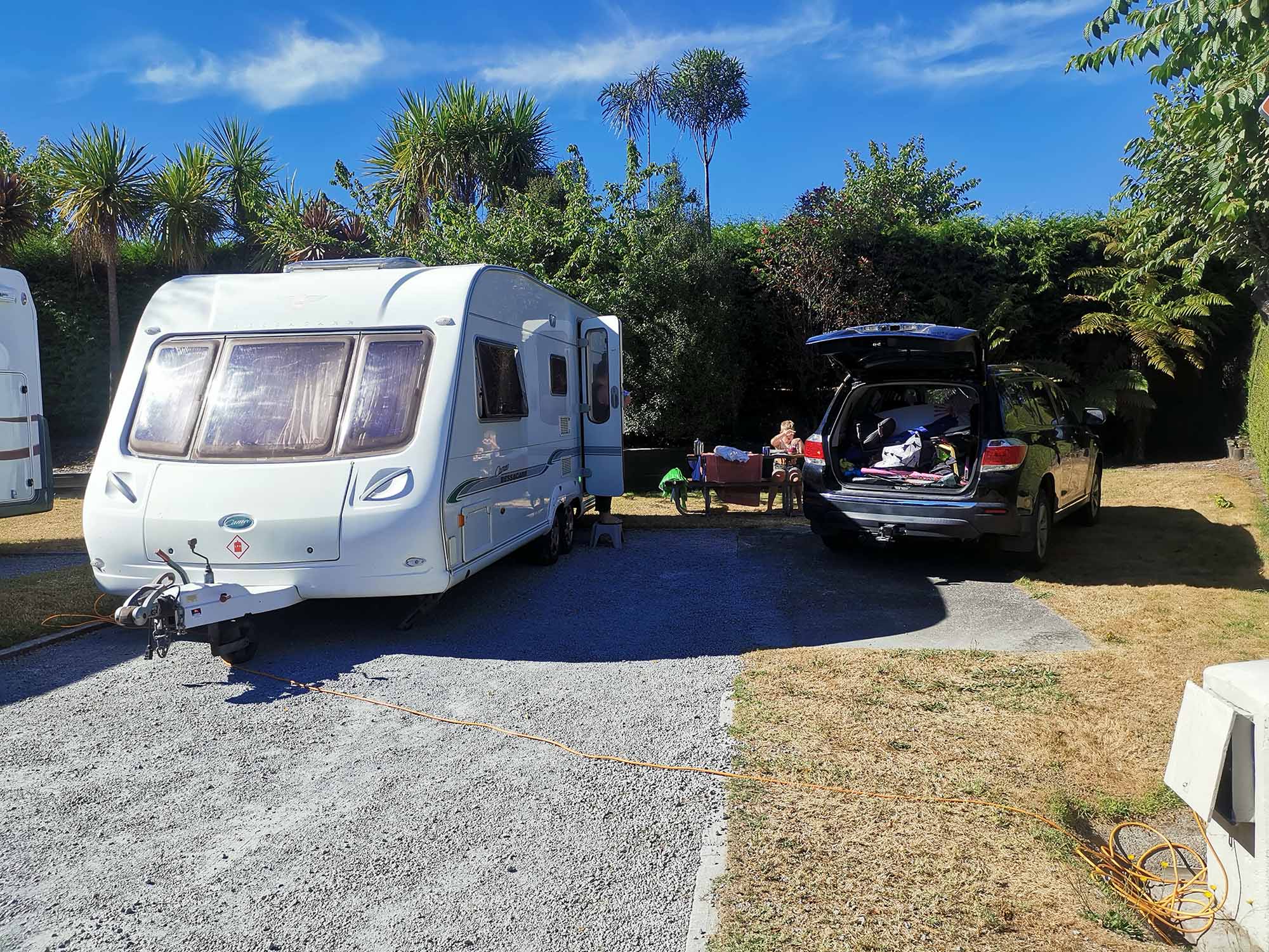 Caravan and car parked on grass in campground in Hawkes Bay NZ, with kids and gear in the background