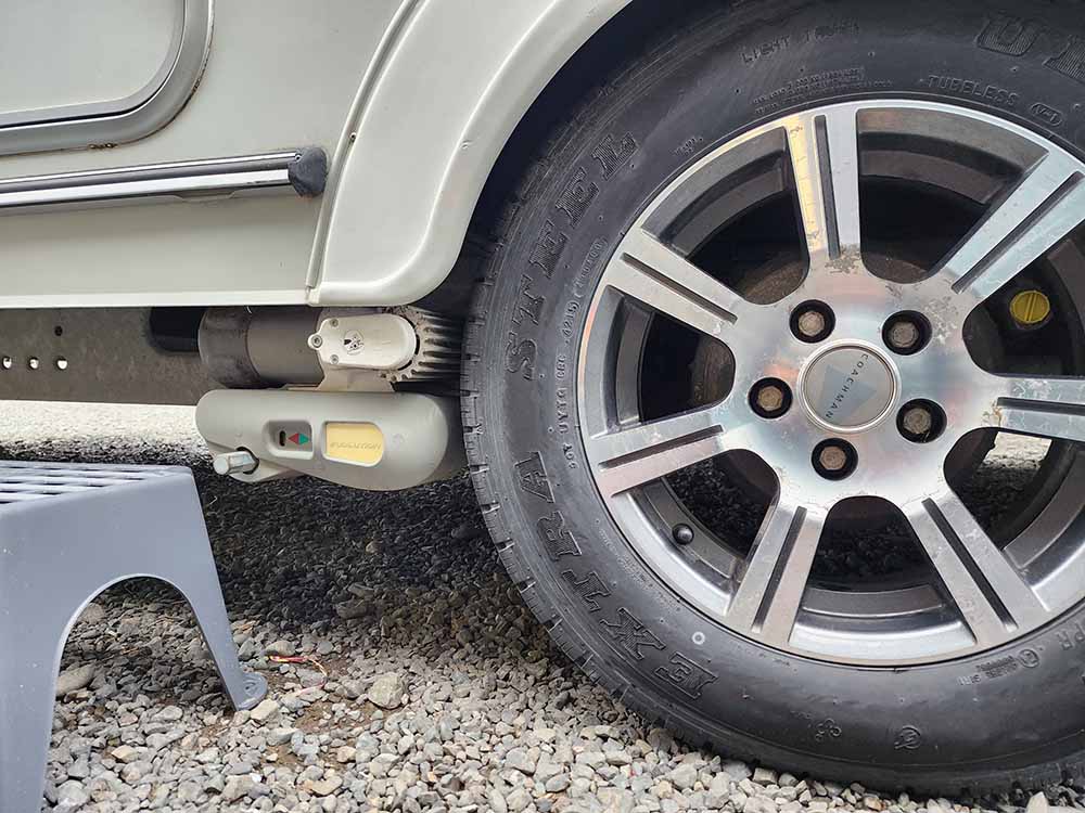 Wheel, step, and chassis of grey caravan parked on gravel