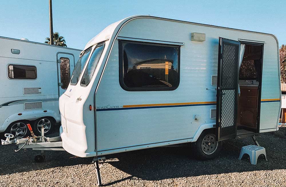 Small white caravan with blue and yellow stripe parked with door open and steps