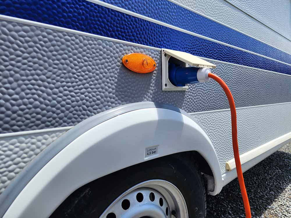Caravan exterior with blue detailing, an orange light and orange power lead connecting to power supply on campground