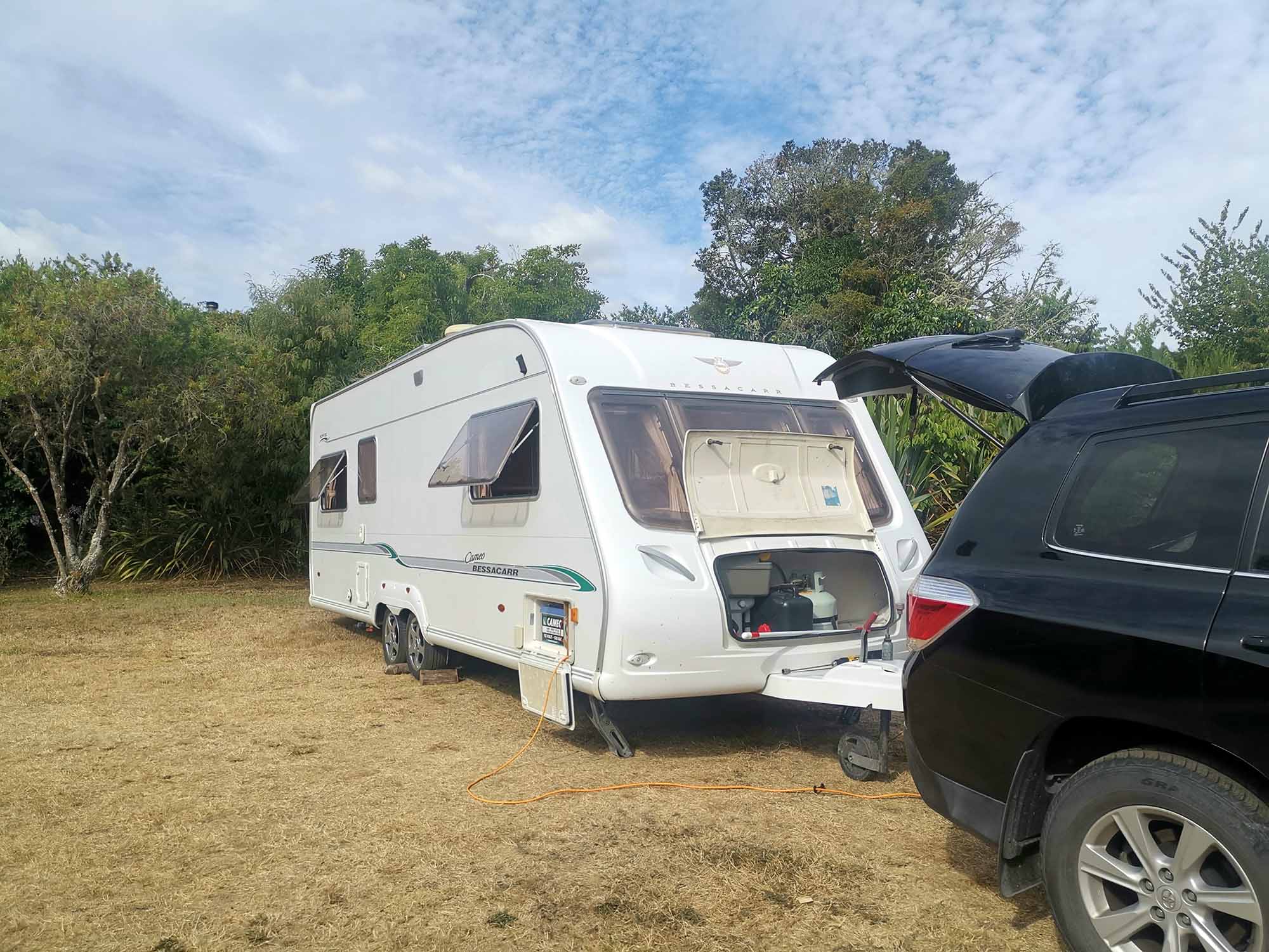 White caravan with windows open on grass field at campground Hawkes Bay - owned by Smile Caravans